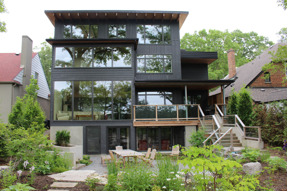 На фото: большой, трехэтажный, серый частный загородный дом в стиле ретро с облицовкой из камня, плоской крышей и зеленой крышей