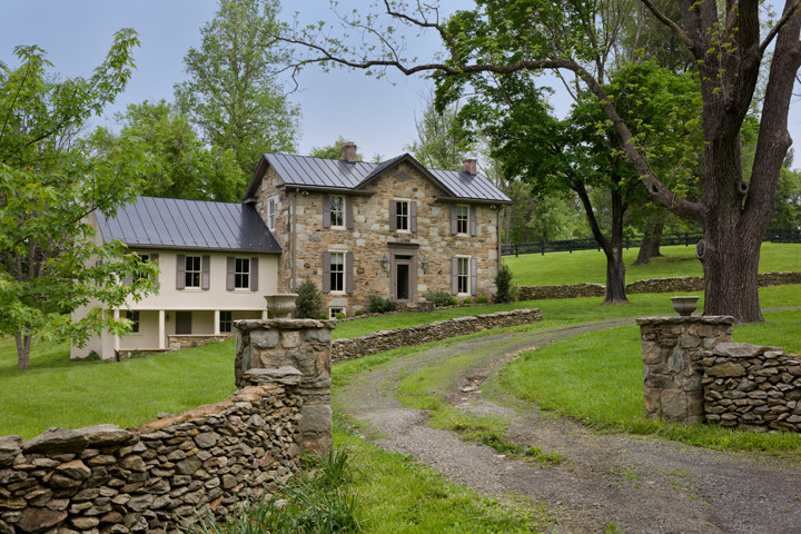 Cette image montre une façade de maison beige rustique en pierre de taille moyenne et à un étage avec un toit à quatre pans.