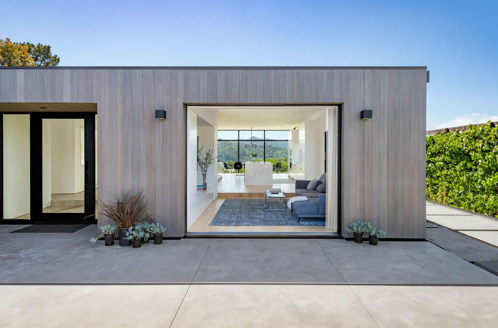 Cette photo montre une façade de maison grise moderne en bois de taille moyenne et de plain-pied avec un toit plat et un toit en métal.