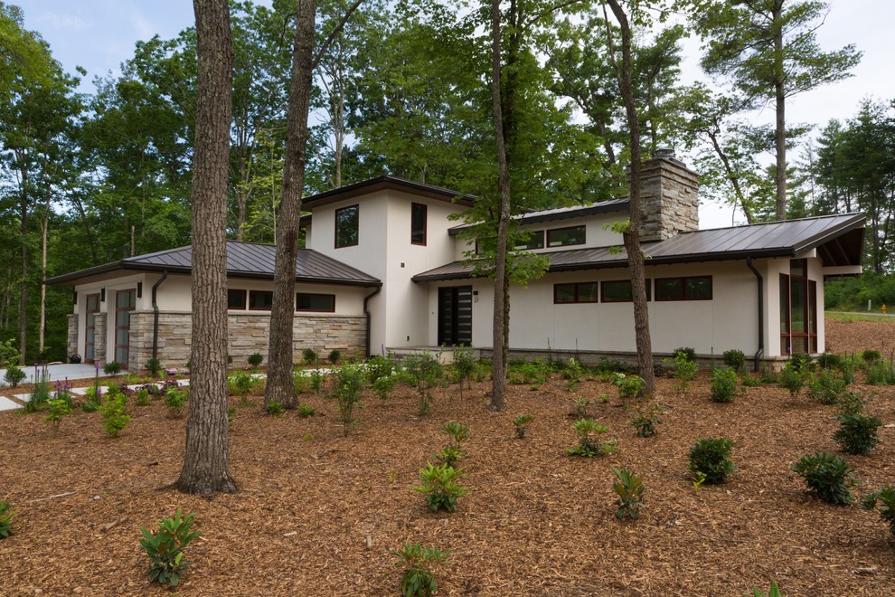 Cette photo montre une façade de maison beige moderne en stuc de taille moyenne et à un étage avec un toit à quatre pans et un toit en métal.