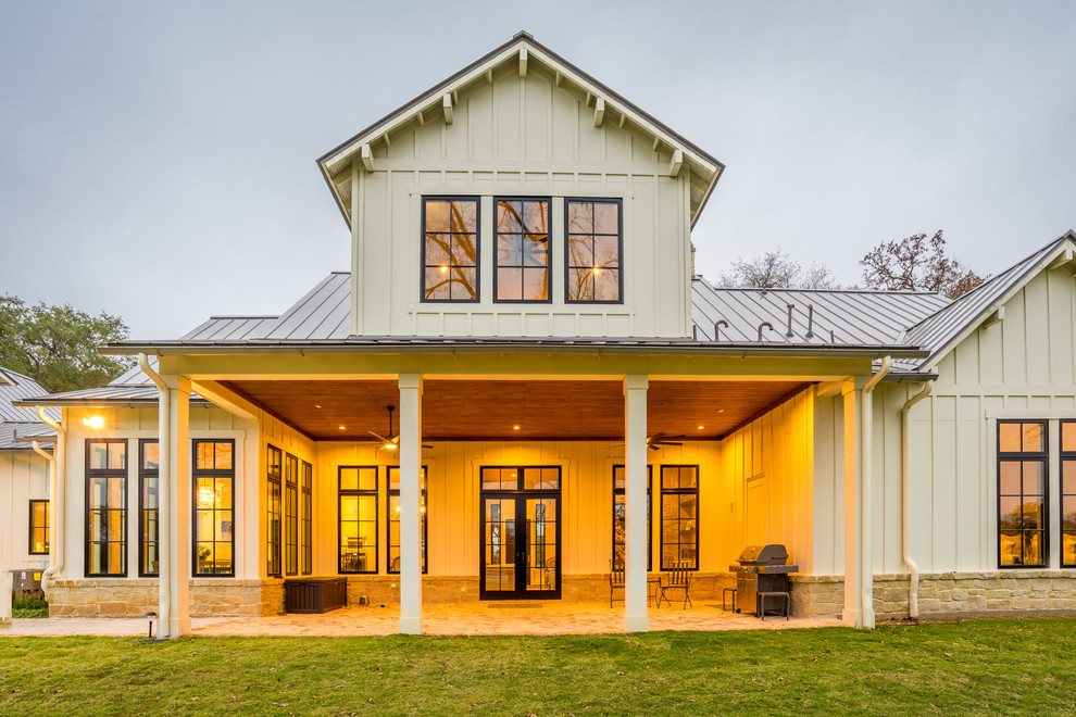 Foto della villa grande beige country a due piani con rivestimento con lastre in cemento, tetto a capanna e copertura in metallo o lamiera