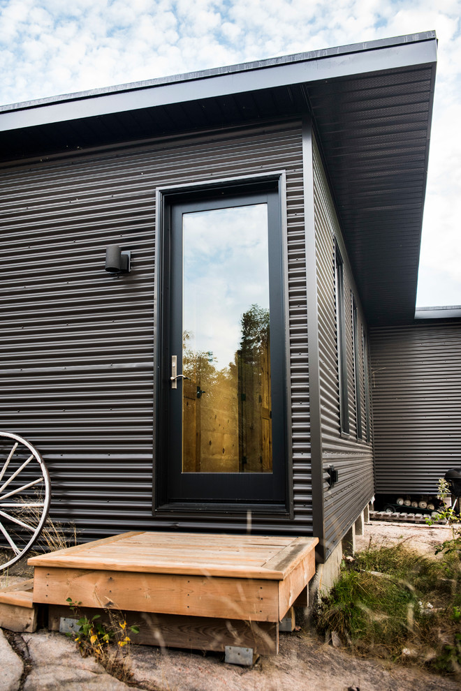 Cette image montre une petite façade de maison métallique et grise urbaine de plain-pied avec un toit plat et un toit en métal.