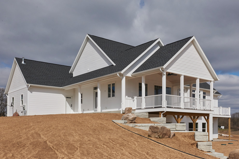 Ejemplo de fachada de casa blanca de estilo de casa de campo grande a niveles con revestimiento de madera, tejado a dos aguas y tejado de teja de madera