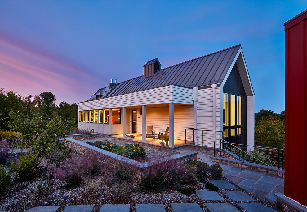 Cette photo montre une grande façade de maison blanche tendance en bois à un étage avec un toit à deux pans et un toit en métal.