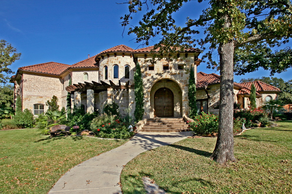Example of a large tuscan beige two-story stone exterior home design in Dallas with a hip roof
