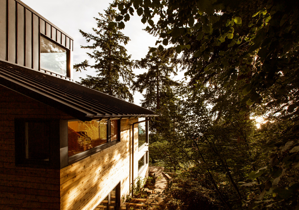 Photo of a large midcentury detached house in Seattle with three floors, wood cladding, a hip roof and a metal roof.