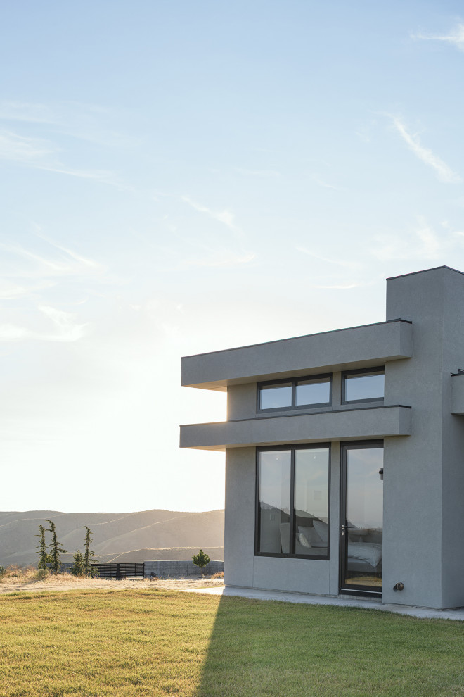 Diseño de fachada de casa gris minimalista grande de una planta con revestimiento de estuco, tejado plano y tejado de metal