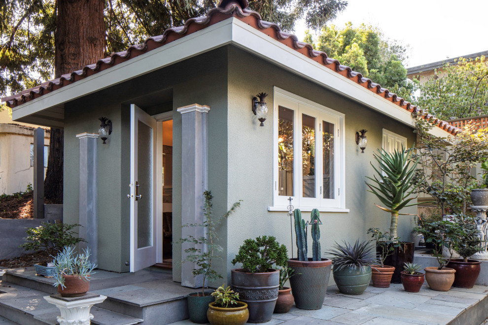 Foto della micro casa piccola verde classica a un piano con rivestimento in stucco, tetto a padiglione, copertura in tegole e tetto marrone