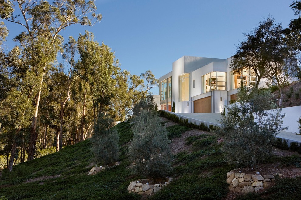 На фото: большой, двухэтажный, белый частный загородный дом в стиле модернизм с облицовкой из цементной штукатурки и плоской крышей