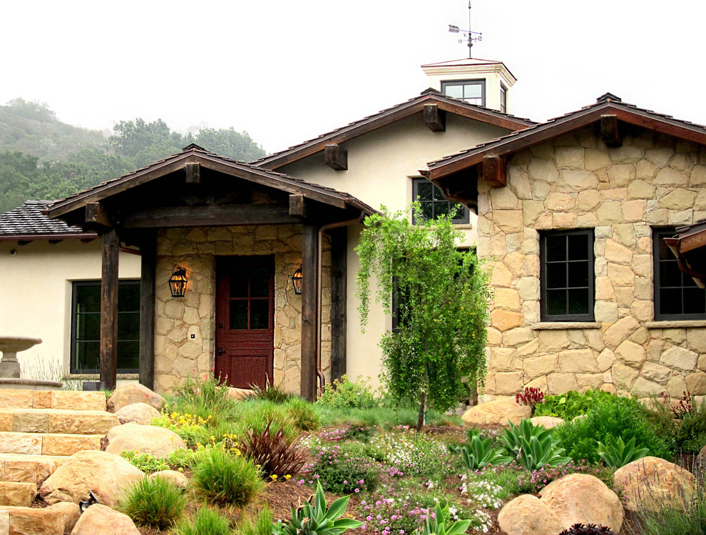 Imagen de fachada de casa beige campestre grande de una planta con revestimiento de piedra, tejado a dos aguas y tejado de teja de barro