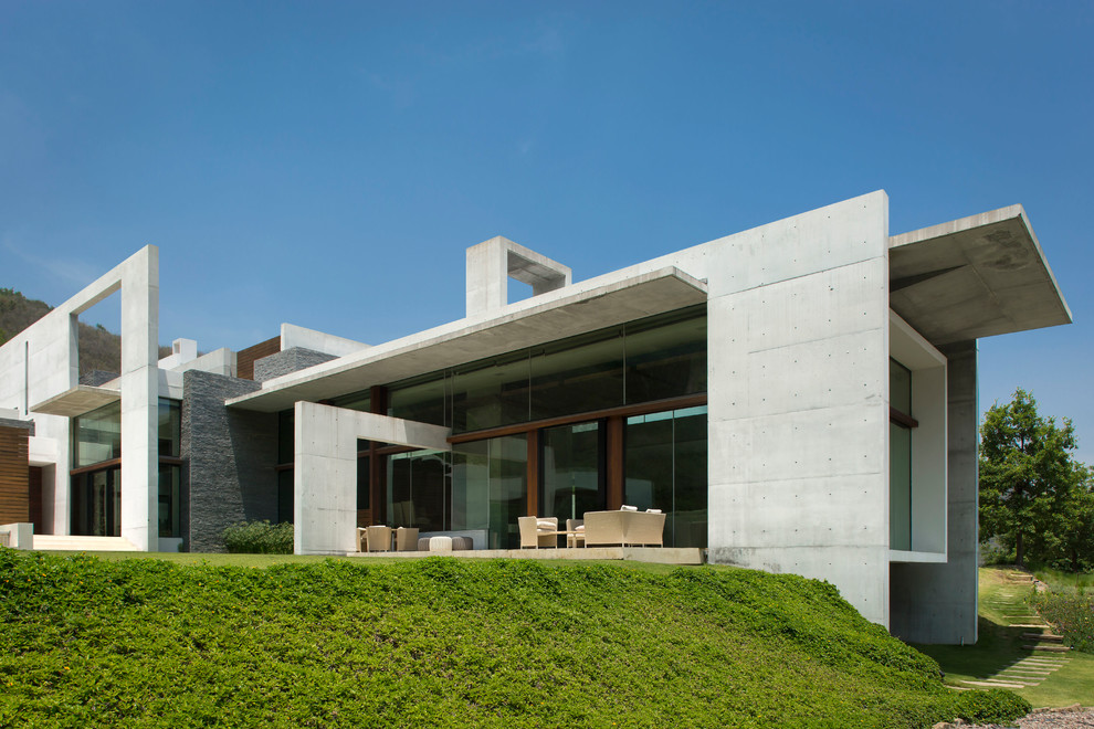 Foto della villa grigia moderna con rivestimento in cemento, tetto piano e terreno in pendenza