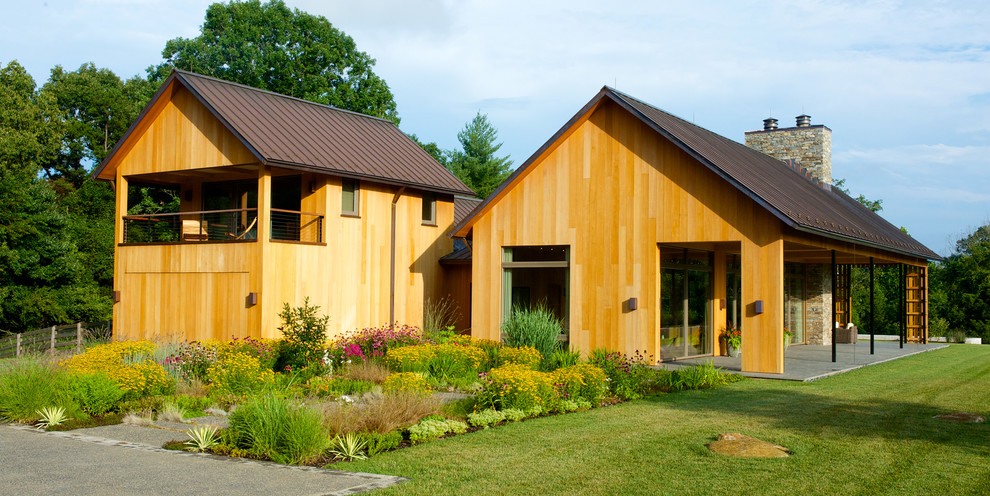 Aménagement d'une grande façade de maison jaune moderne en bois à un étage avec un toit à deux pans et un toit en métal.