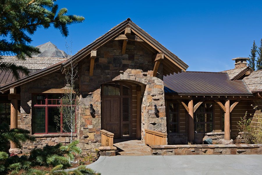 Large mountain style brown two-story stone house exterior photo in Other with a shingle roof