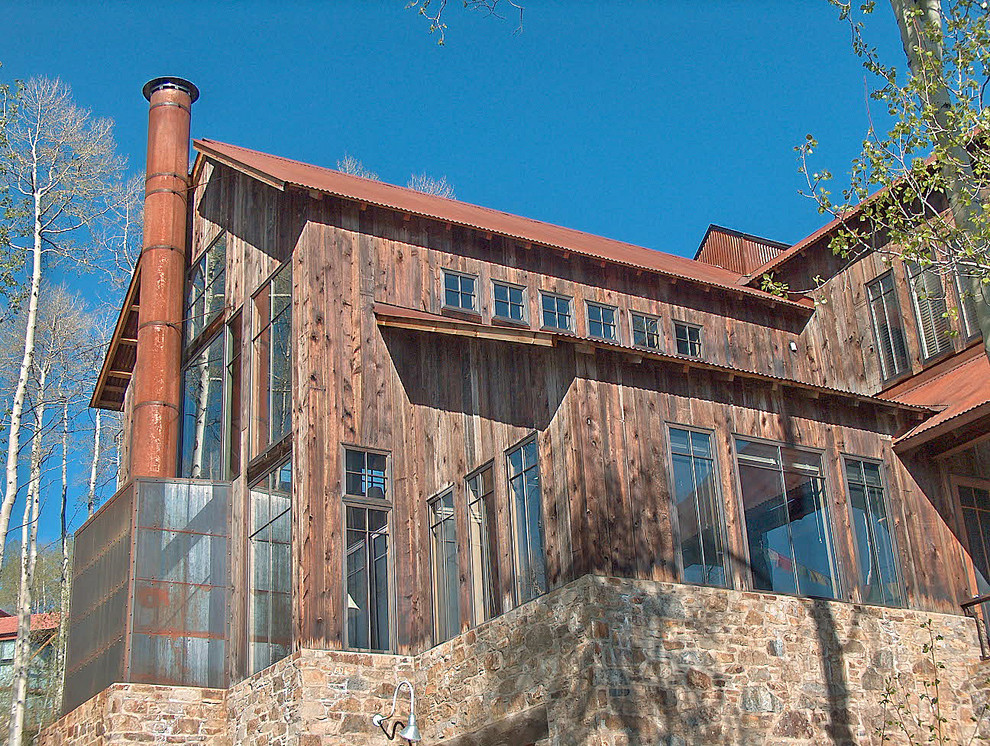 Immagine della villa grande marrone rustica a tre piani con rivestimento in legno, tetto a capanna e copertura in metallo o lamiera