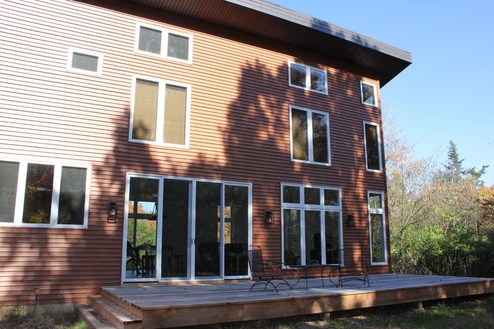 Réalisation d'une façade de maison rouge minimaliste à un étage avec un revêtement en vinyle, un toit en appentis et un toit en shingle.