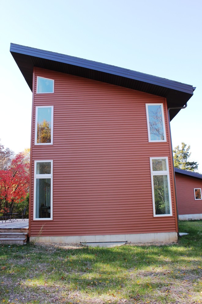 Foto på ett funkis rött hus, med två våningar, vinylfasad, pulpettak och tak i shingel