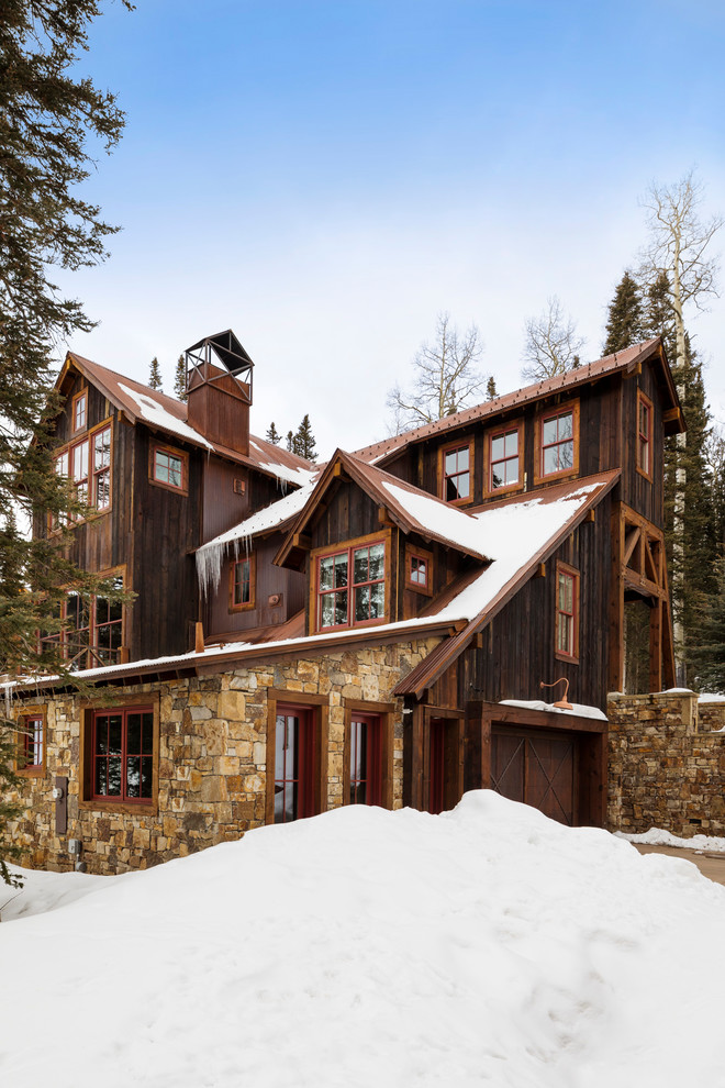 Modelo de fachada de casa marrón rural grande de tres plantas con revestimientos combinados, tejado a dos aguas y tejado de metal