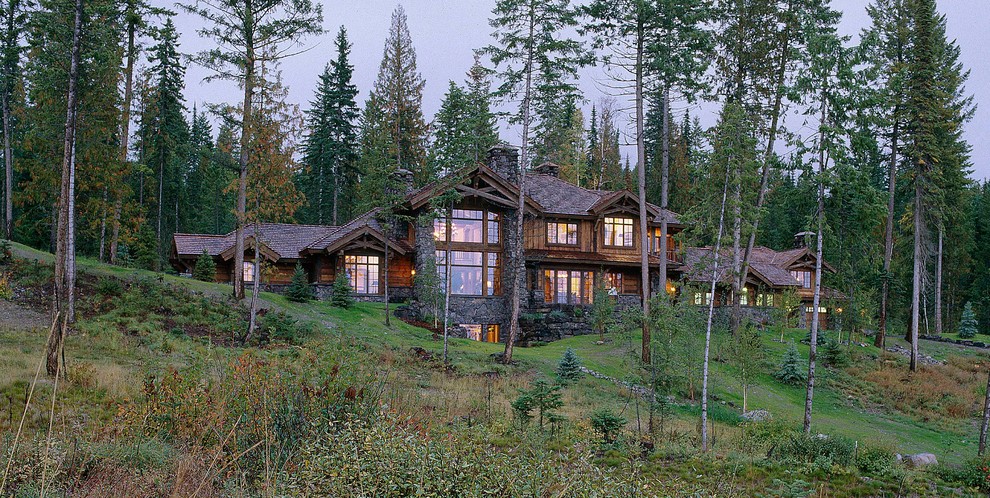 На фото: огромный, трехэтажный, деревянный, коричневый частный загородный дом в стиле рустика с двускатной крышей и крышей из гибкой черепицы