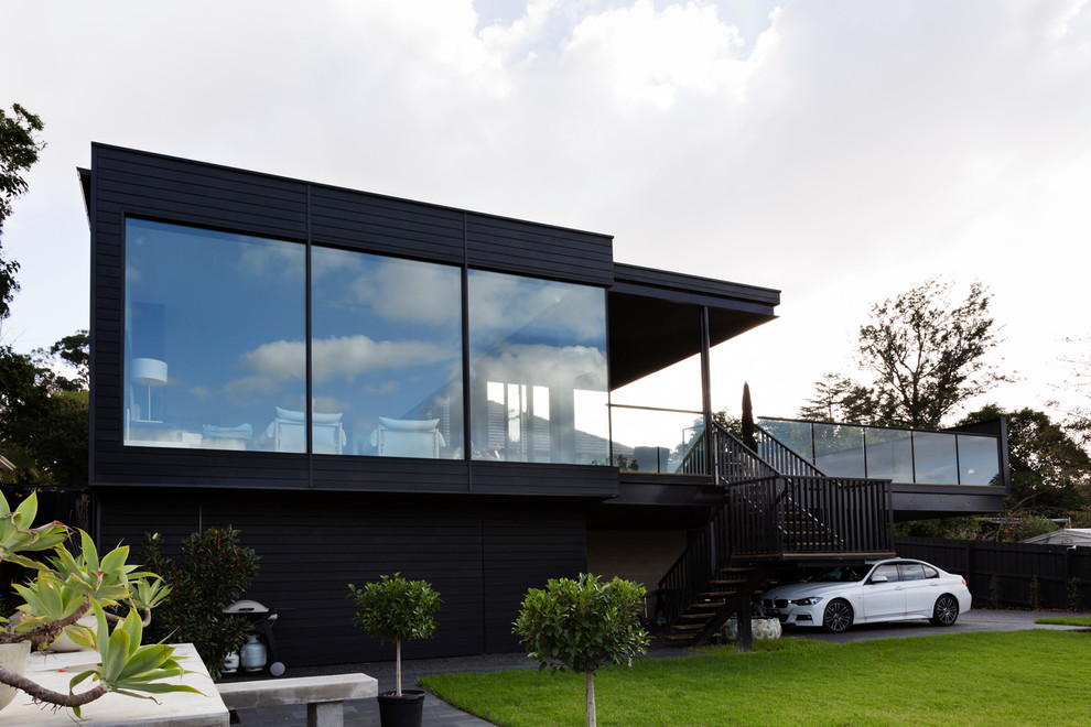 Immagine della facciata di una casa grande nera scandinava a due piani con rivestimento in legno e tetto piano