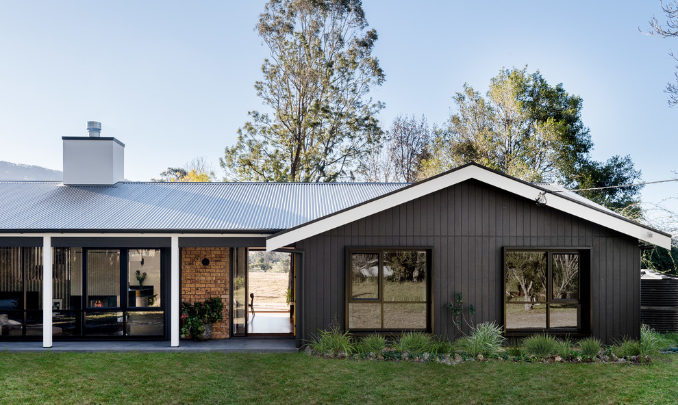 Réalisation d'une grande façade de maison noire vintage de plain-pied avec un revêtement mixte, un toit à deux pans et un toit en métal.