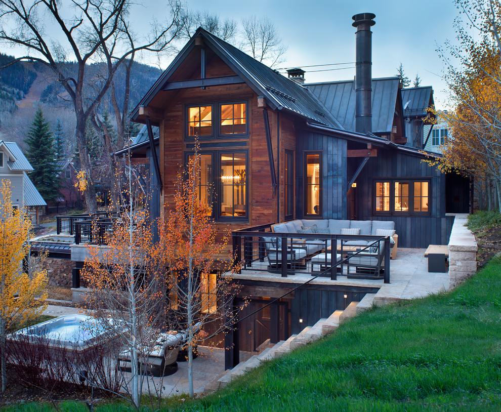 На фото: коричневый дом в стиле рустика с разными уровнями, комбинированной облицовкой и двускатной крышей