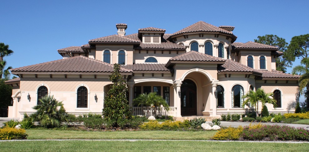 Cette image montre une grande façade de maison beige méditerranéenne en stuc à un étage avec un toit à quatre pans.