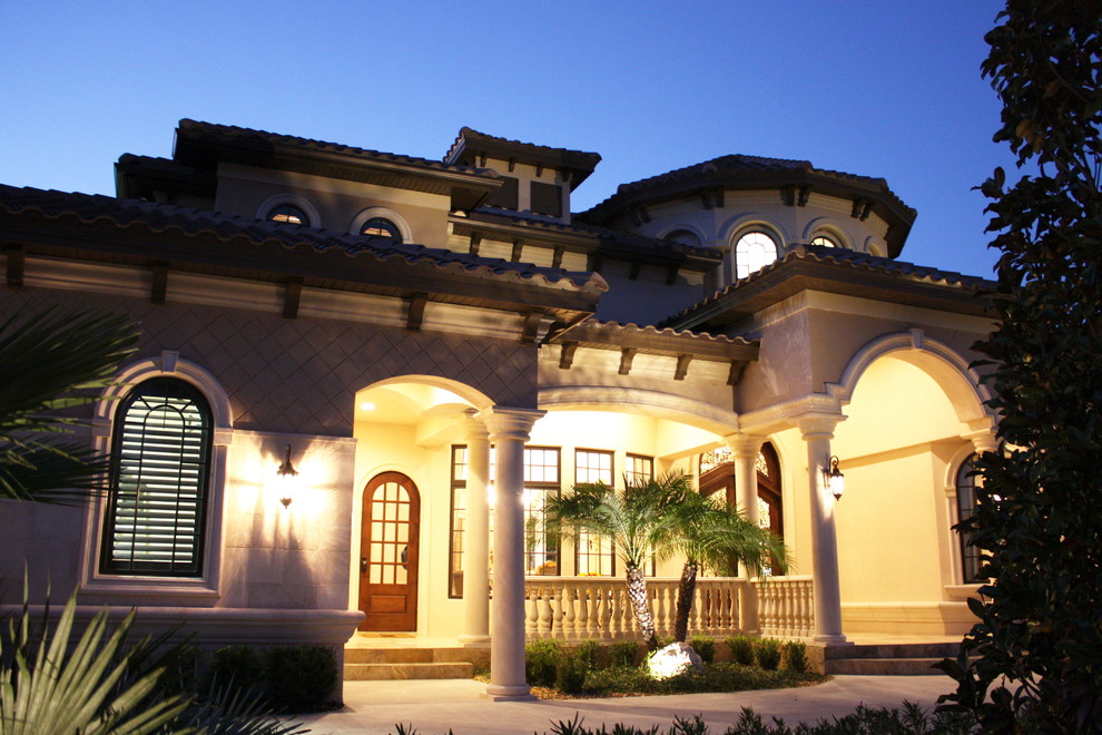 Exemple d'une grande façade de maison beige méditerranéenne en stuc à un étage avec un toit à quatre pans.