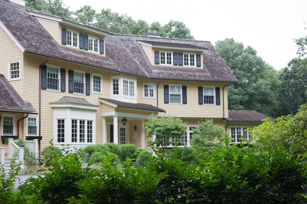 Immagine della facciata di una casa grande gialla classica a tre piani con rivestimento in legno
