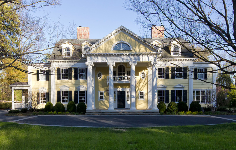 Foto della villa ampia gialla classica a tre piani con rivestimento in stucco, tetto a mansarda e copertura a scandole