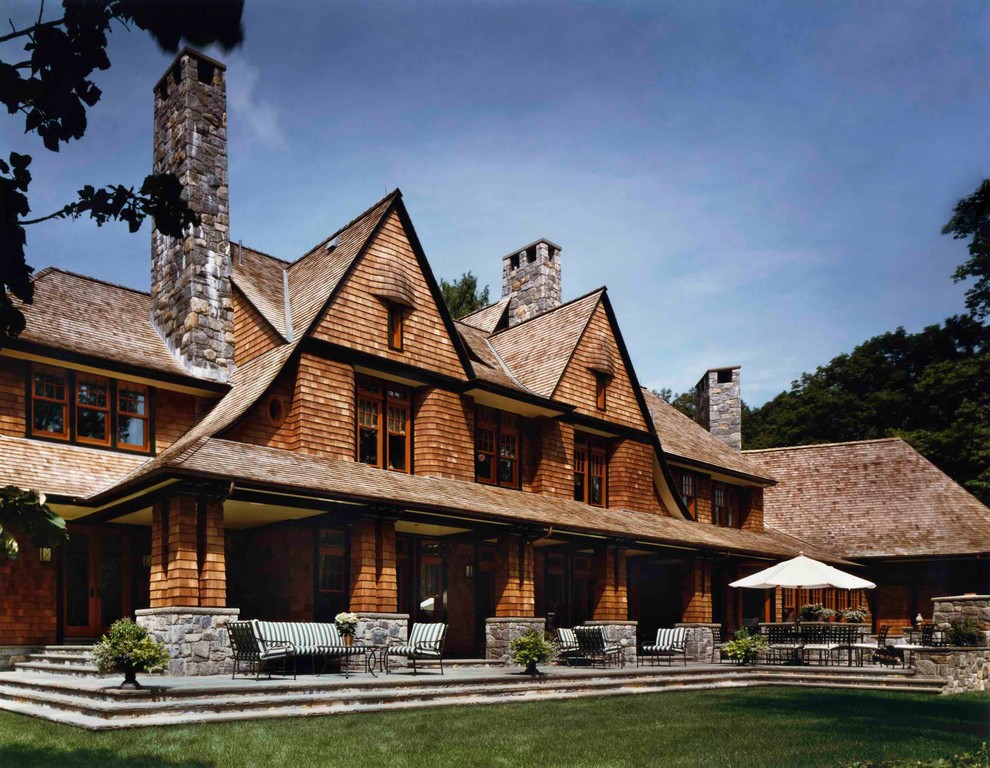 Esempio della villa ampia marrone rustica a due piani con rivestimento in legno, tetto a capanna e copertura a scandole