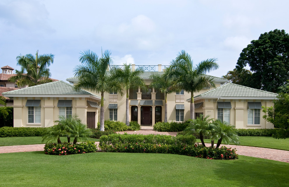 Ejemplo de fachada de casa beige exótica grande de dos plantas con revestimiento de estuco, tejado a cuatro aguas y tejado de teja de barro