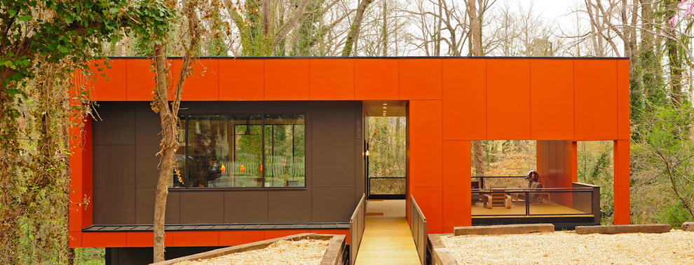 Aménagement d'une grande façade de maison orange et métallique moderne à un étage avec un toit plat, un toit en métal et un toit noir.