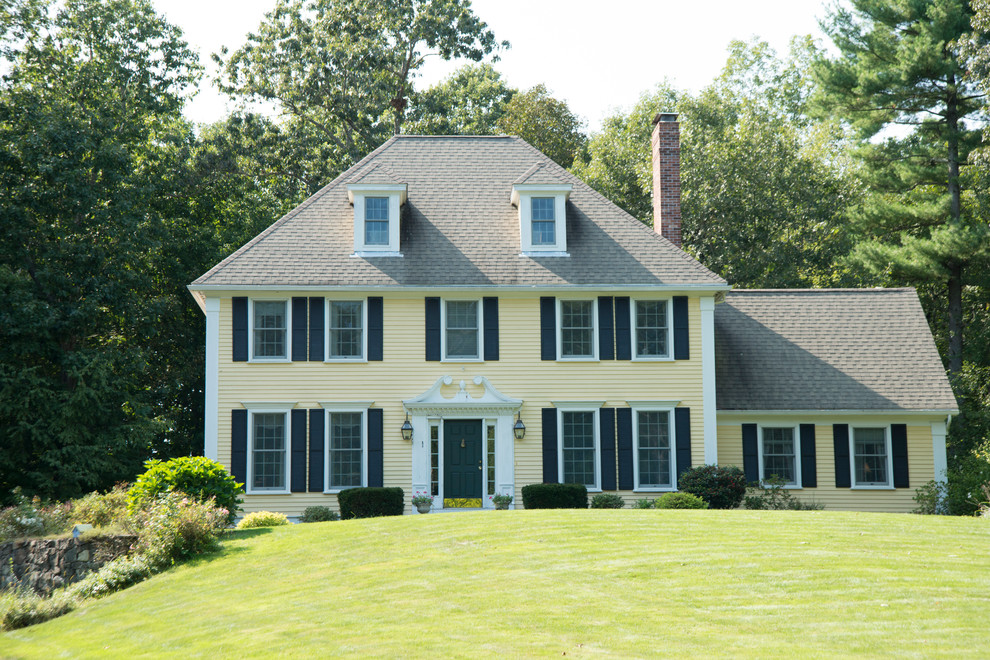 Aménagement d'une façade de maison jaune classique en bois de taille moyenne et à un étage avec un toit à quatre pans.