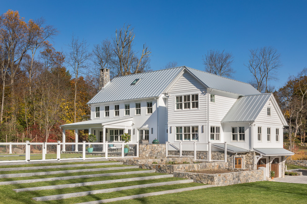 На фото: большой, двухэтажный, белый частный загородный дом в стиле кантри с комбинированной облицовкой, двускатной крышей и металлической крышей с