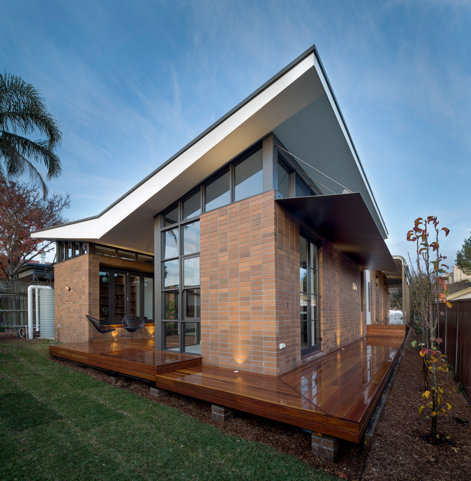 Mid-sized elegant brown one-story brick house exterior photo in Sydney with a hip roof and a metal roof