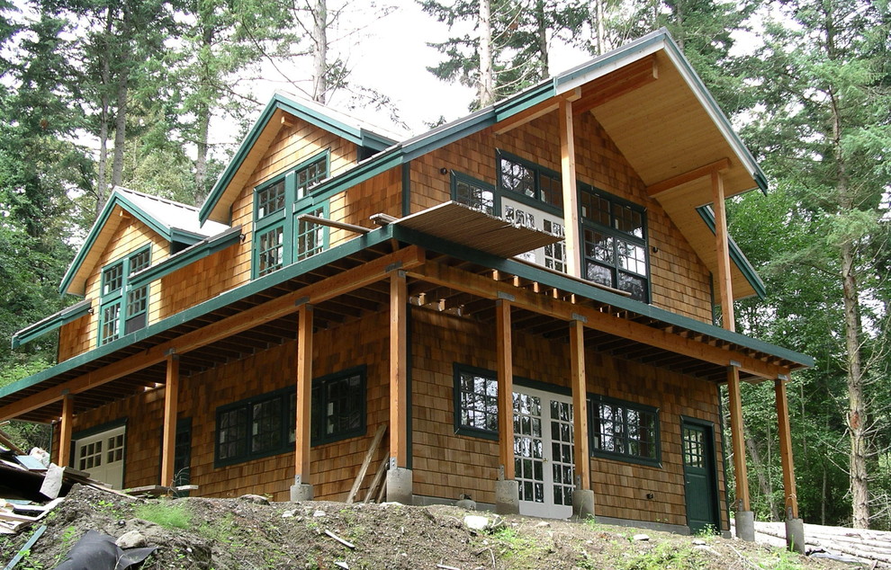 Esempio della villa piccola marrone rustica a due piani con rivestimento in legno, tetto a capanna e copertura in metallo o lamiera