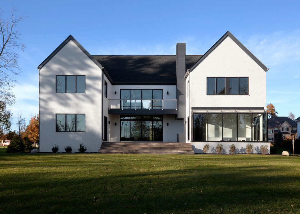 Cette photo montre une grande façade de maison blanche en brique à un étage avec un toit à deux pans et un toit en shingle.