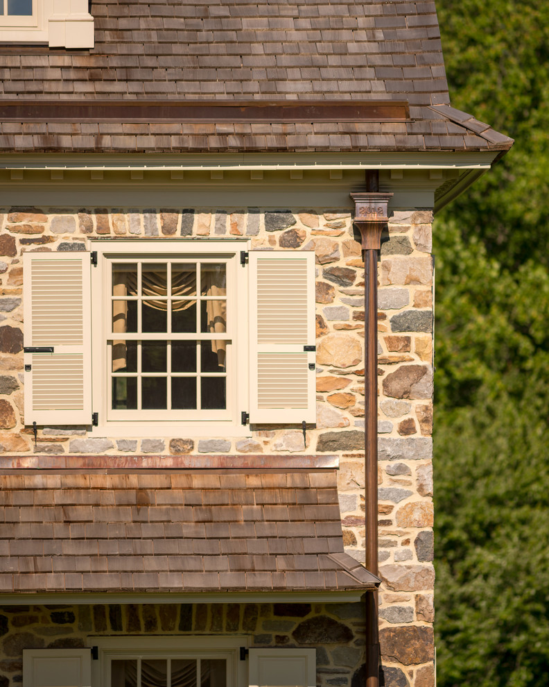 Esempio della facciata di una casa beige country a due piani con rivestimento in pietra e tetto a capanna