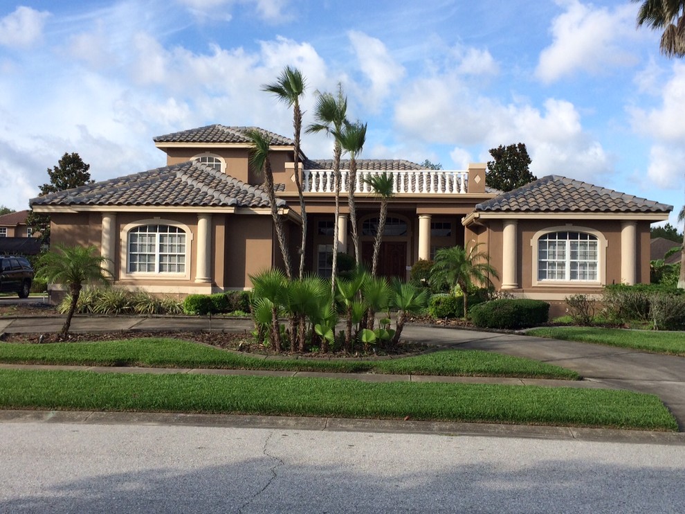 Large island style brown two-story stucco exterior home photo in Tampa with a hip roof and a tile roof