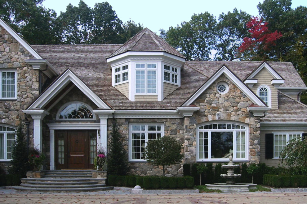 Aménagement d'une grande façade de maison beige classique en pierre à un étage avec un toit en shingle.