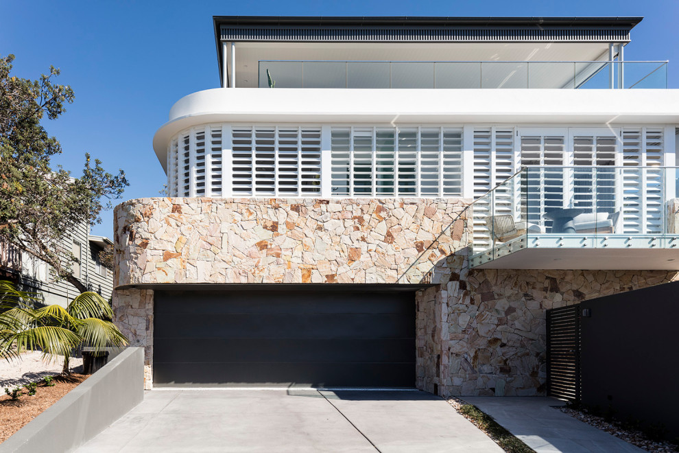 This is an example of a large and white nautical detached house in Sunshine Coast with three floors, stone cladding, a hip roof and a metal roof.