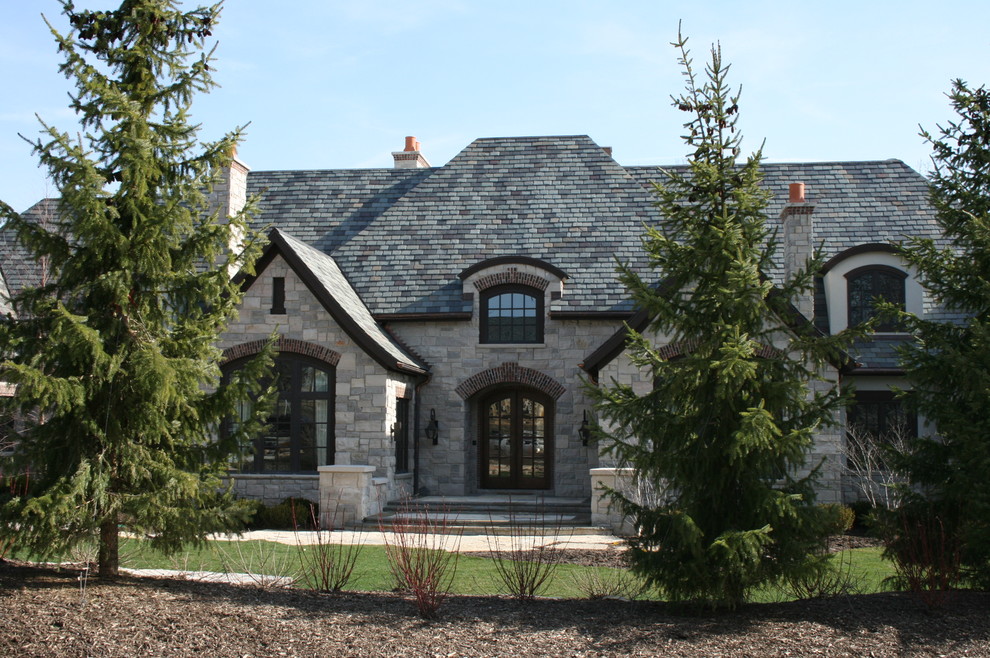 Esempio della facciata di una casa grande grigia classica a due piani con rivestimento in pietra, tetto a capanna e abbinamento di colori