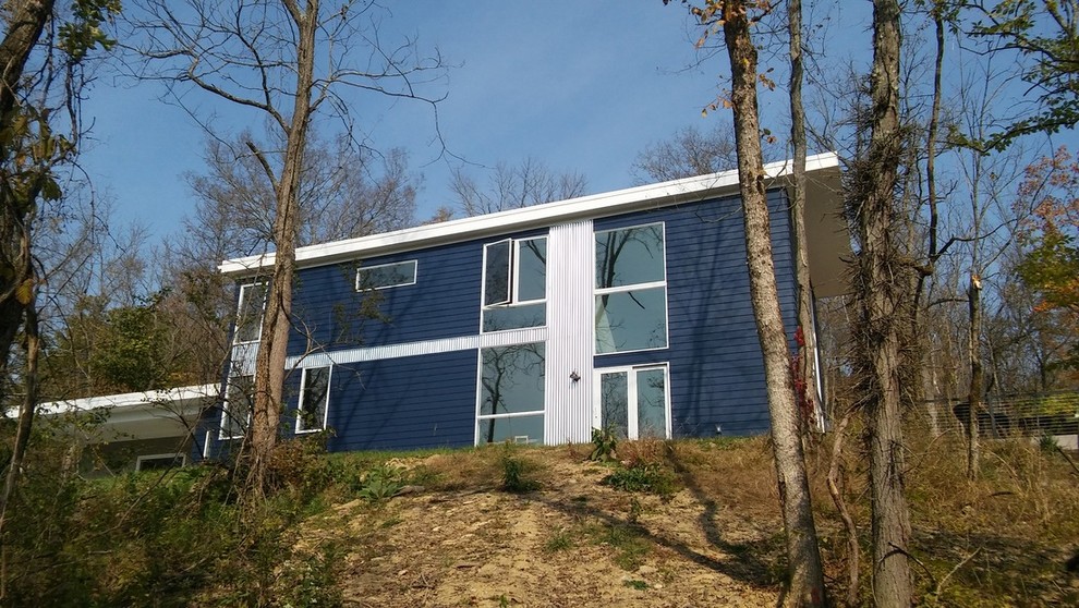 Cette photo montre une façade de maison bleue moderne de taille moyenne et à un étage avec un revêtement en vinyle et un toit plat.