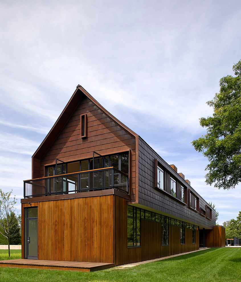 На фото: двухэтажный, коричневый дом в стиле кантри с комбинированной облицовкой и двускатной крышей