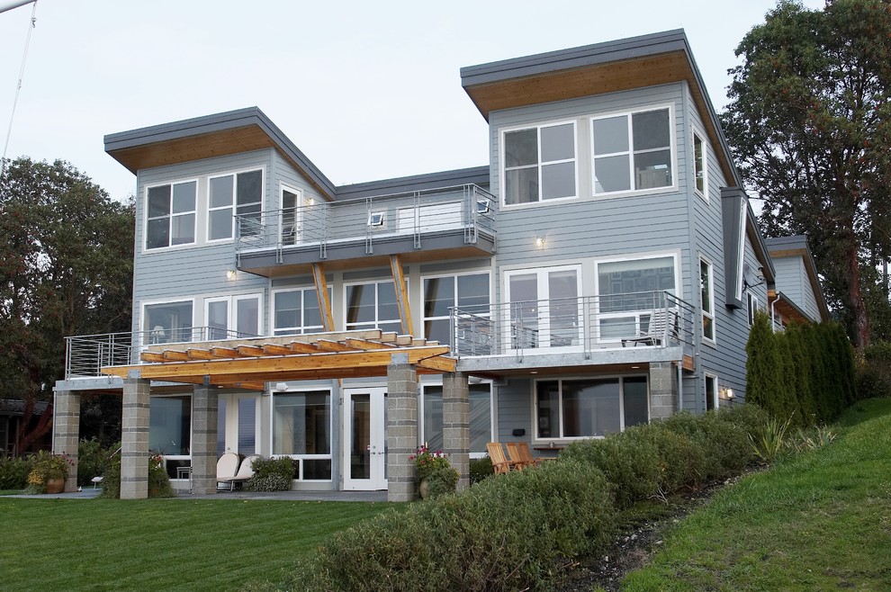 Foto på ett mellanstort funkis grått hus, med tre eller fler plan, fiberplattor i betong, pulpettak och tak i metall