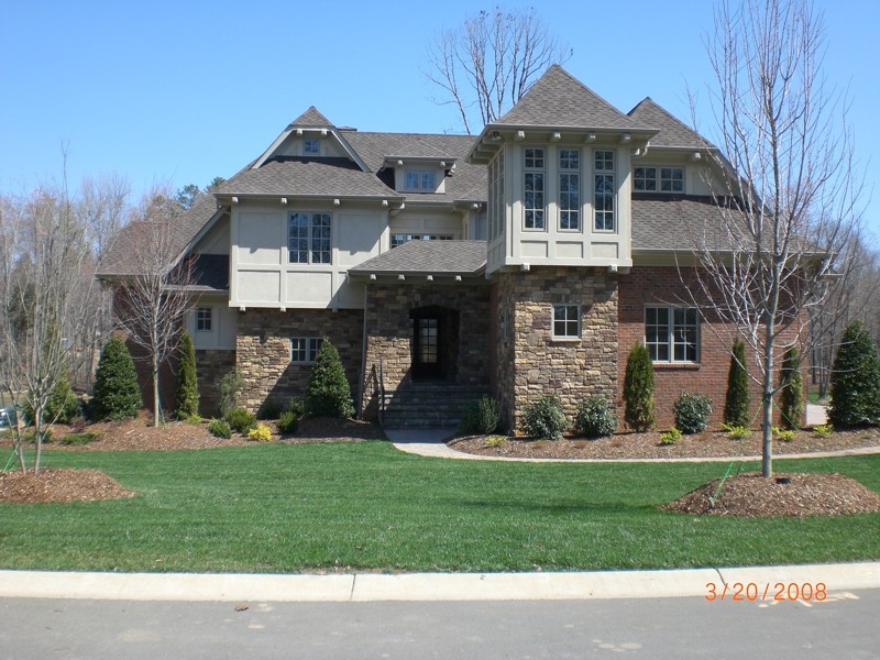 This is an example of a large and beige world-inspired house exterior in Charlotte with three floors, stone cladding and a half-hip roof.