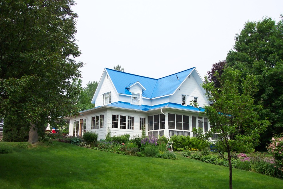 Foto della villa grande bianca country a due piani con rivestimento in legno, tetto a capanna, copertura in metallo o lamiera e tetto blu