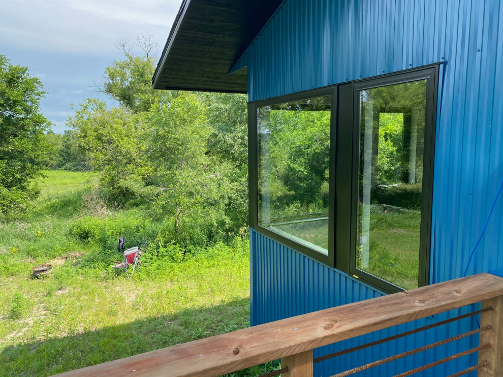 Cette photo montre une façade de maison métallique et bleue tendance à un étage avec un toit à deux pans et un toit en shingle.