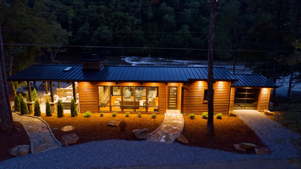 Cette image montre une façade de maison marron chalet en bois de taille moyenne et de plain-pied avec un toit à deux pans et un toit en métal.