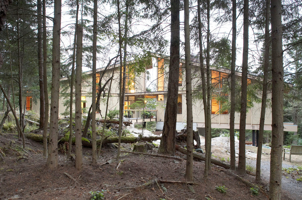 Cette image montre une grande façade de maison beige design en bois à niveaux décalés avec un toit en appentis.